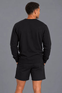Male model showcasing the plain back of the XX-XY Athletics Crewneck Sweatshirt, paired with black shorts against a gray studio background || Black