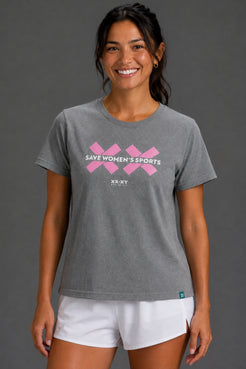 A woman wearing a heather gray short-sleeve t-shirt with a pink graphic that reads 'SAVE WOMEN'S SPORTS' and 'XX-XY SPORTS' underneath, paired with white athletic shorts, against a solid gray studio background. || Heather Gray