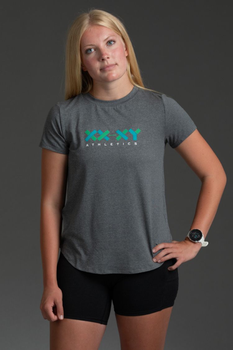 Woman wearing a gray t-shirt with a logo and black shorts on a dark background