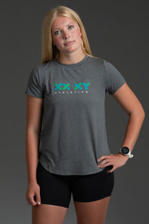 Woman wearing a gray t-shirt with a logo and black shorts on a dark background || Black/Dark Heather Gray/White
