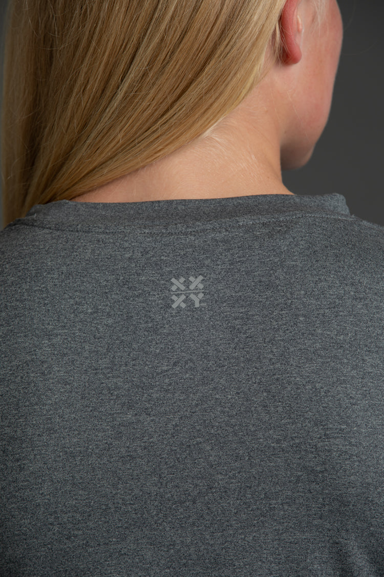 A woman modeling a heather gray athletic t-shirt with a white 'XX XY ATHLETICS' logo on the back against a dark gray studio background.
