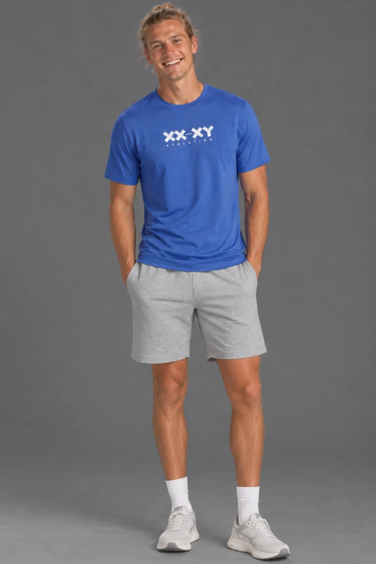 Blonde male model with a man bun laughing in the blue XX-XY Athletics Logo Tee and gray shorts.