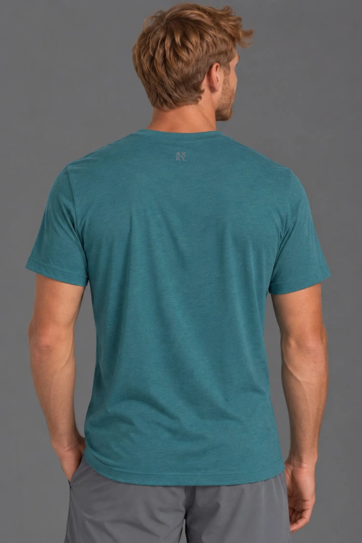 A man viewed from behind wearing a teal heathered short-sleeve t-shirt and gray shorts against a solid gray studio background. || Teal Green
