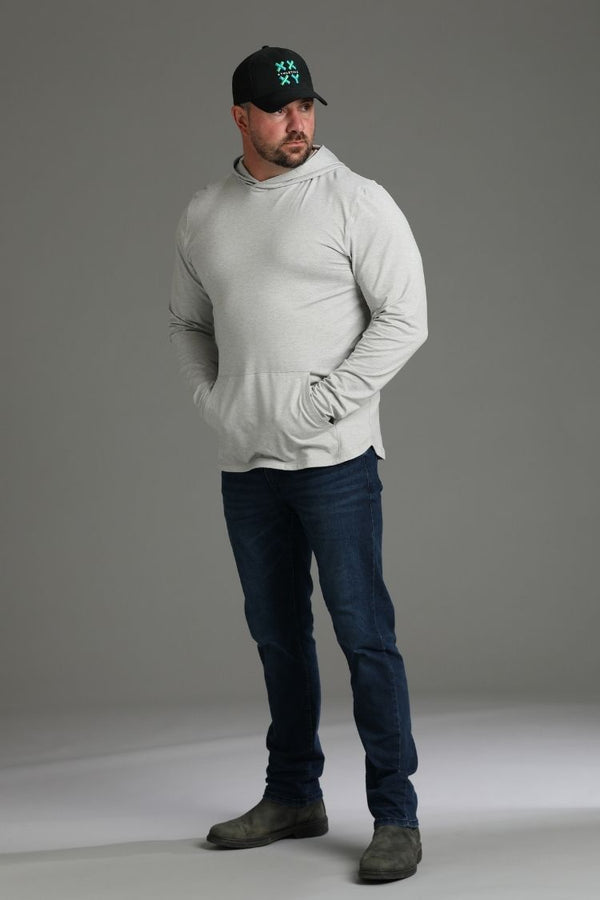 Man wearing a light gray hoodie, dark jeans, and a black cap with a logo on a gray background || light heather gray - 1