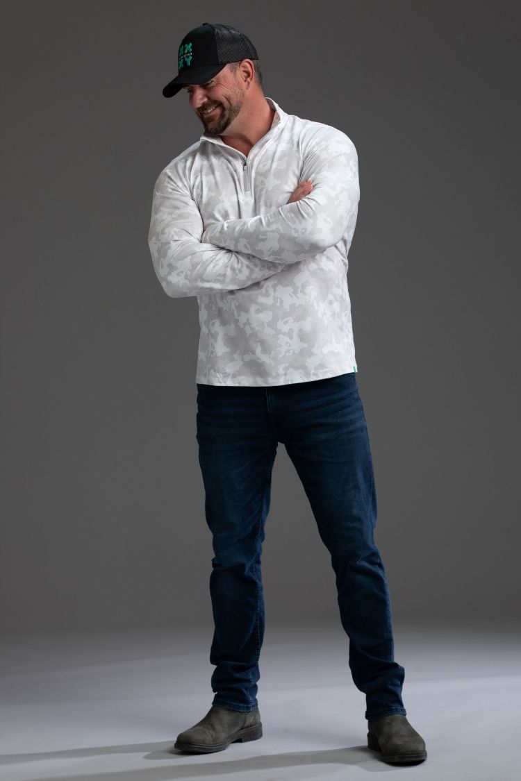 Man wearing a white long-sleeve shirt, dark jeans, and a black cap with a logo || white camo