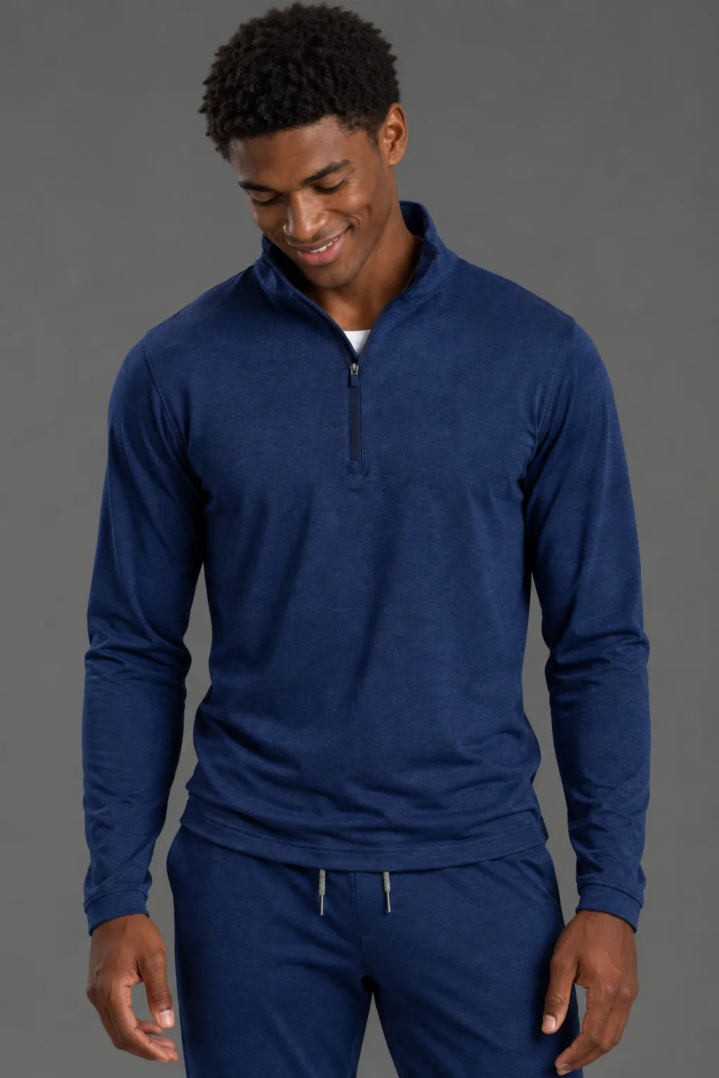 A man wearing a navy blue long-sleeve quarter-zip pullover and matching navy pants, standing against a solid dark gray studio background. || Navy