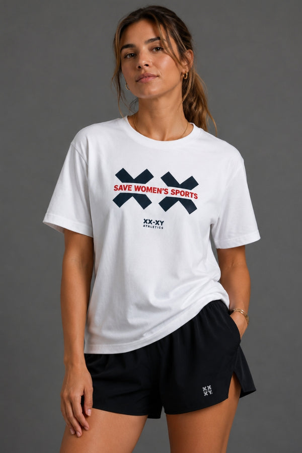 A woman wearing a white short-sleeve graphic T-shirt and black athletic shorts, standing against a plain gray studio background. The shirt has a navy and red 'SAVE WOMEN'S SPORTS' graphic with 'XX-XY' branding. || White
