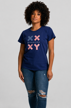 A woman with curly black hair wearing a navy blue short-sleeve t-shirt with a red, white, and blue graphic on the front, paired with blue jeans, against a light gray studio background. || Navy