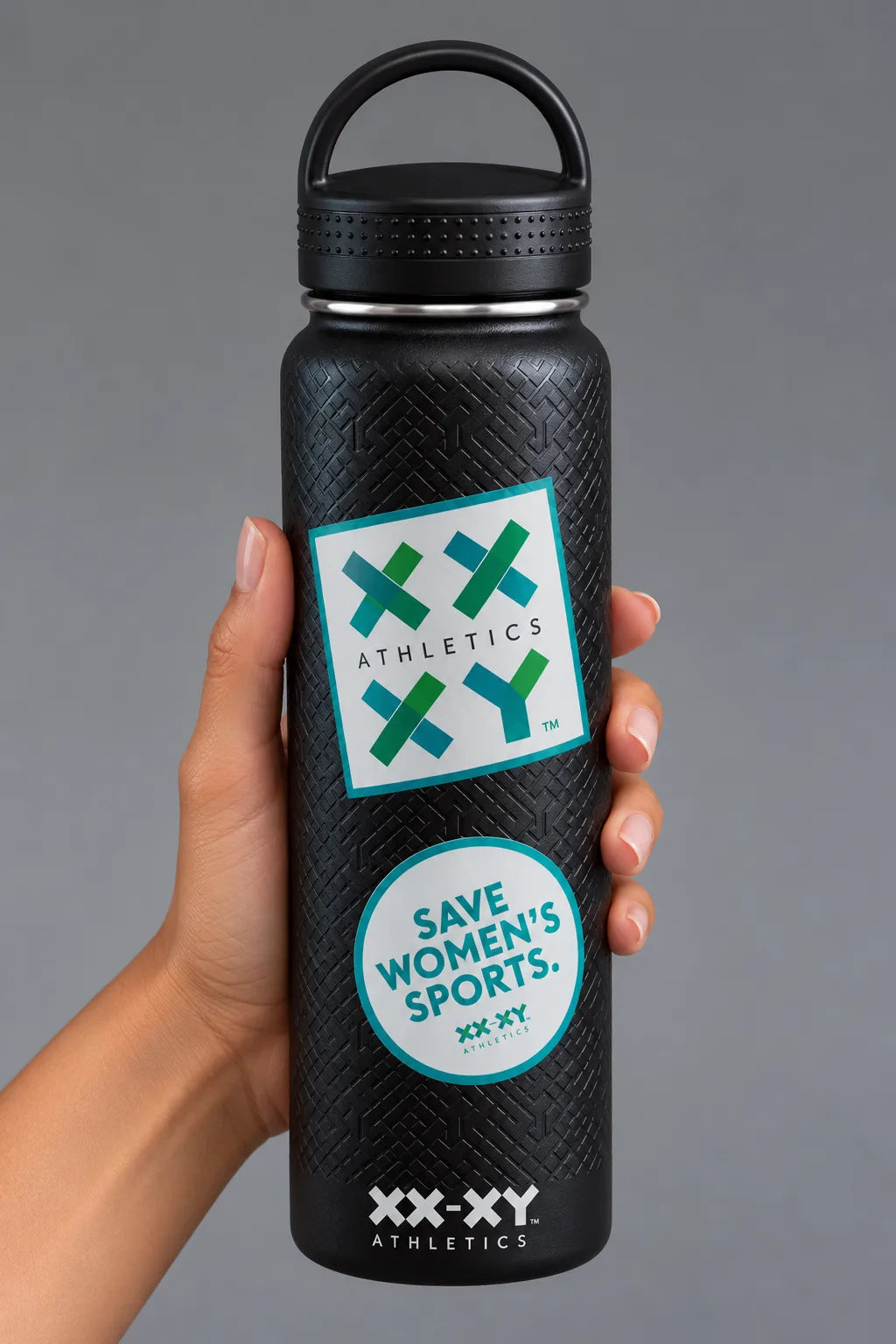 Hand holding black XX-XY Athletics water bottle with Athletics logo and Save Women’s Sports stickers on gray background