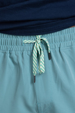Teal shorts with a green and white striped drawstring on a person wearing a navy top. || Underseas