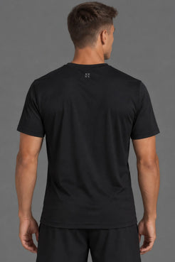 A man viewed from the back wearing a black short-sleeve athletic t-shirt with a small white logo centered below the collar, paired with black shorts, against a solid gray studio background. || Black