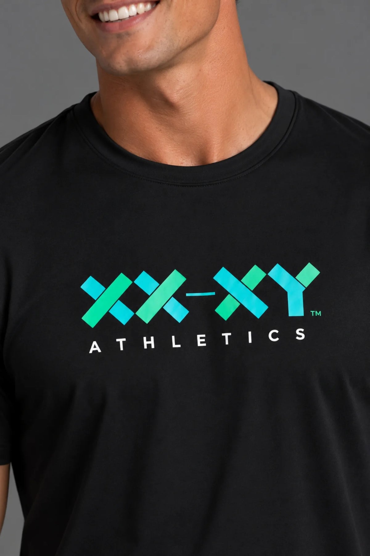Close-up of the teal and green XX-XY Athletics logo on the black men’s performance tee.
