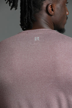 Close-up back view of a person wearing a heathered mauve-pink knit top, showing the neck, hair, and a small white geometric logo centered below the neckline. || Burgundy Heather