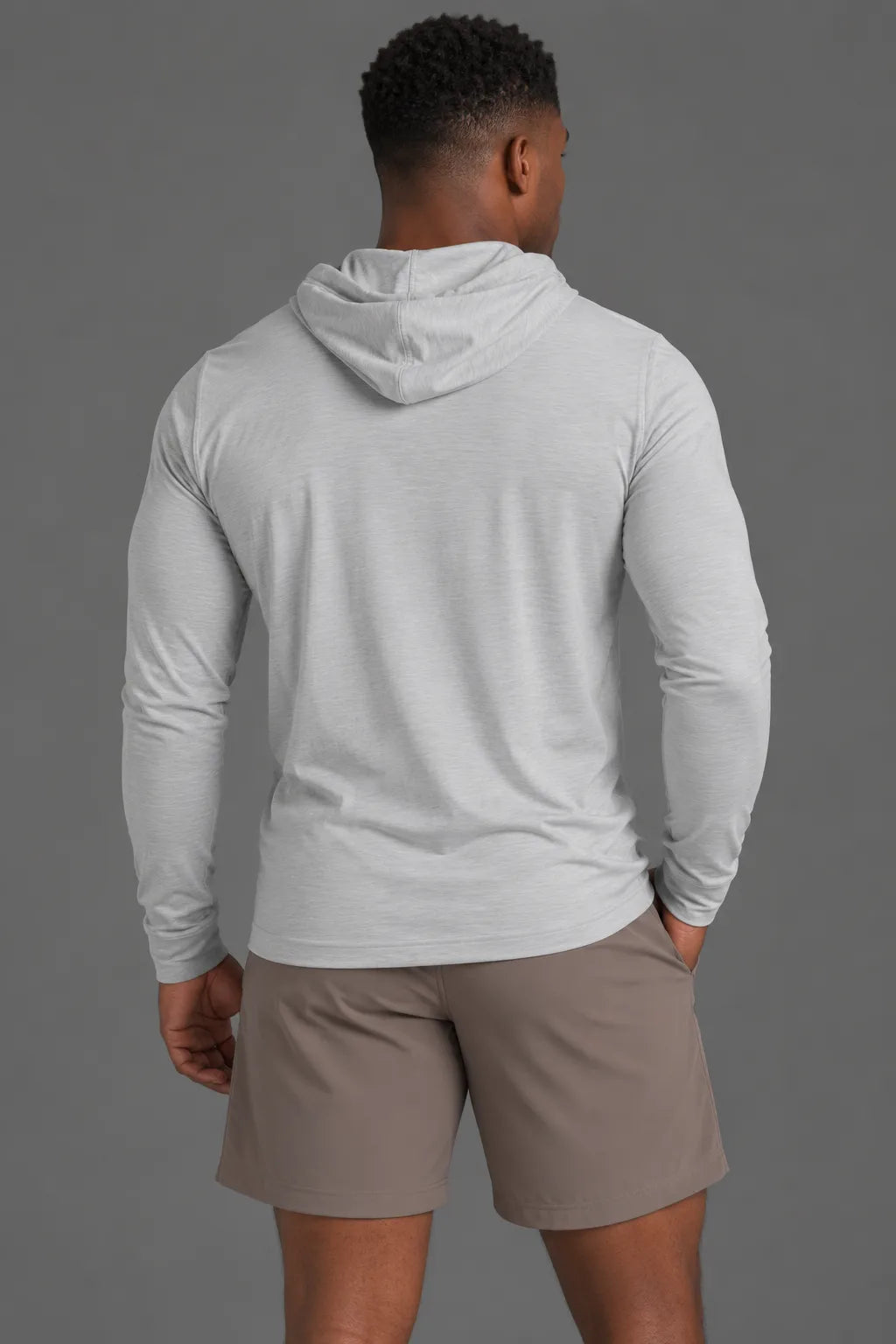 Back view of a Black male model wearing a light gray performance hoodie with brown athletic shorts. || Light Heather Gray - 1