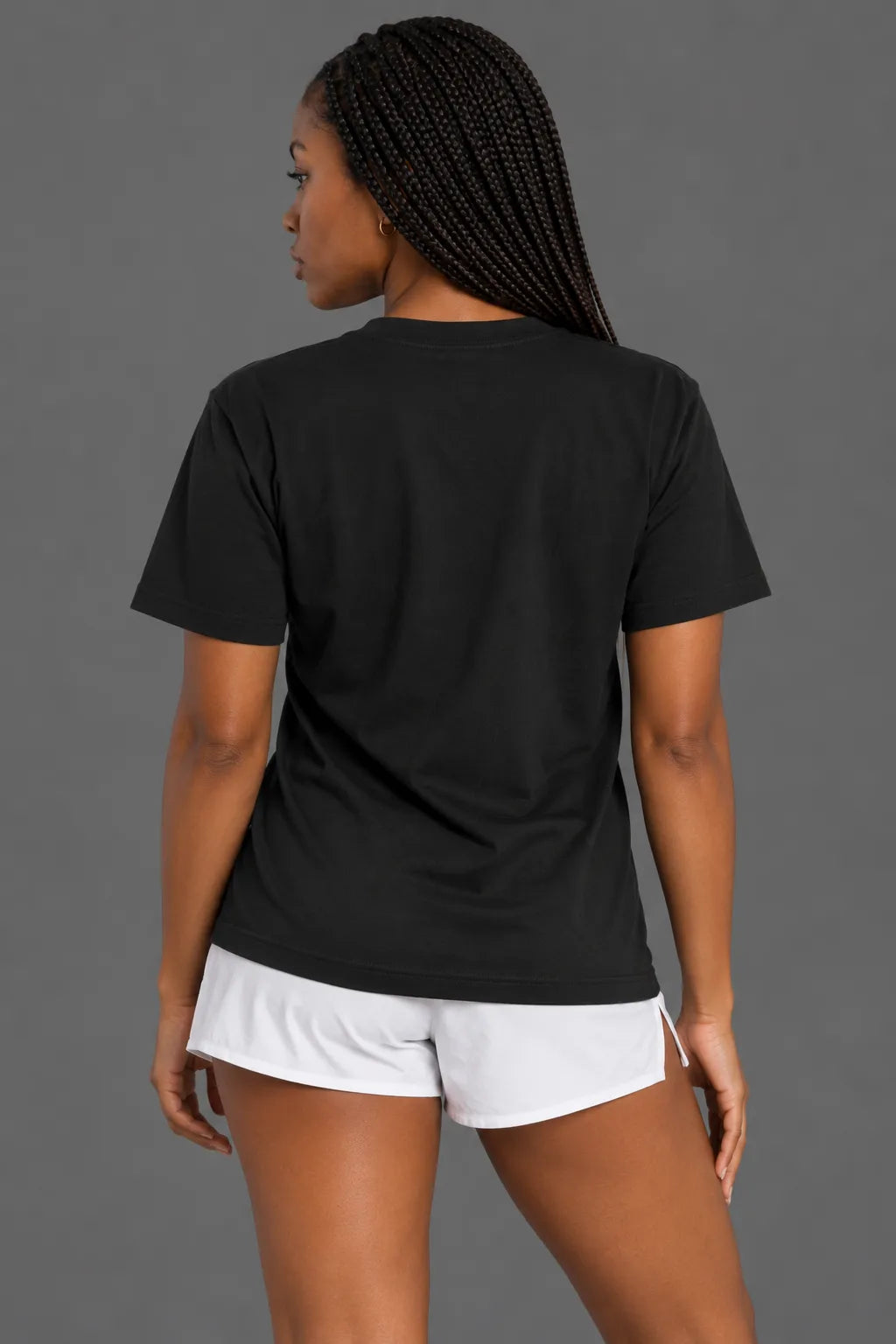 Back view of female model wearing black XX-XY Athletics t-shirt with plain back and white athletic shorts against gray background. || Black