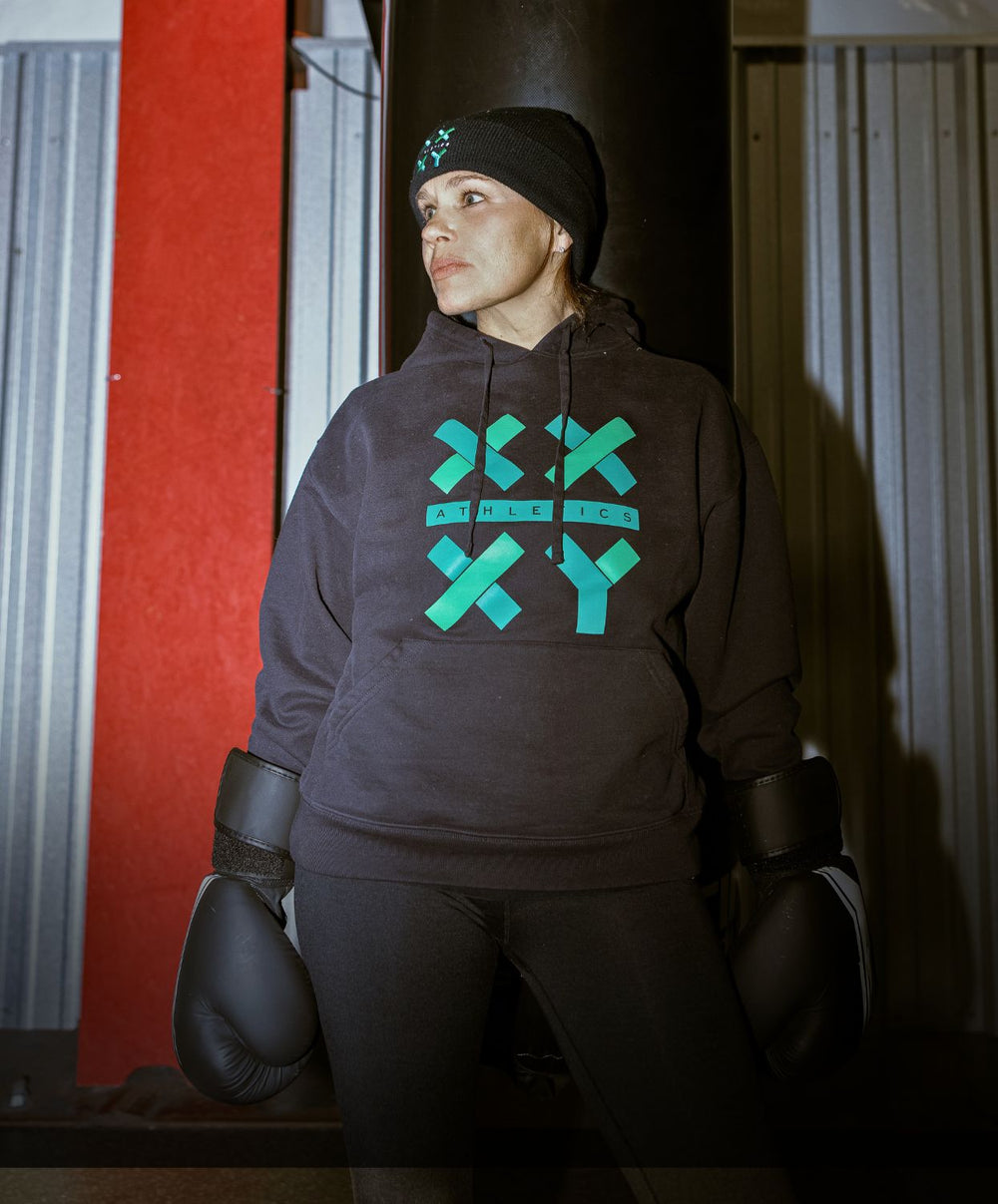Person wearing a dark hoodie with green logo in a gym setting