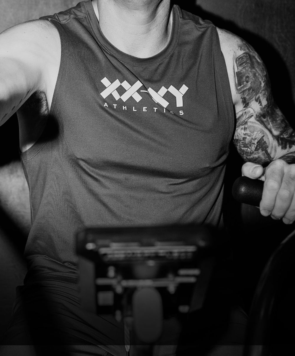 Person wearing a tank top with 'XXXY Athletics' logo on a gym machine.