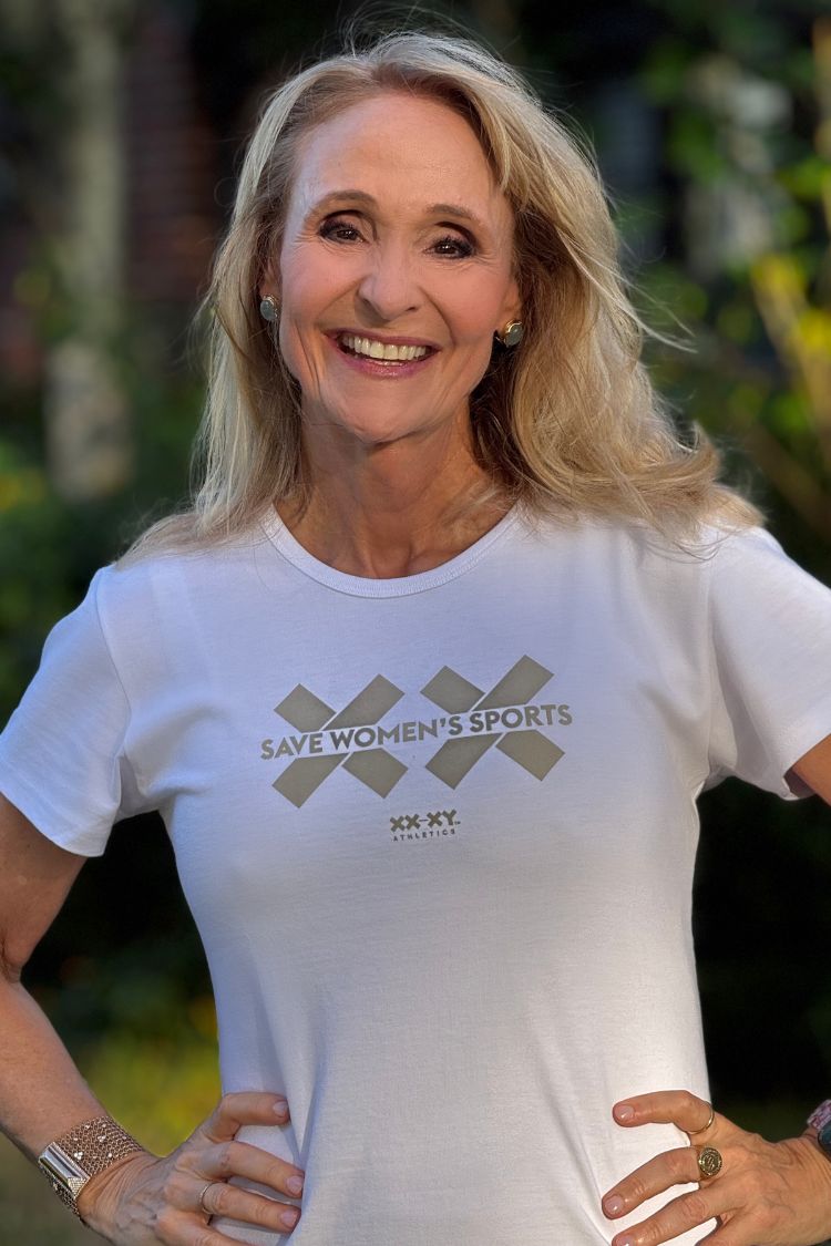 Woman wearing a white t-shirt with a logo and text, standing outdoors.