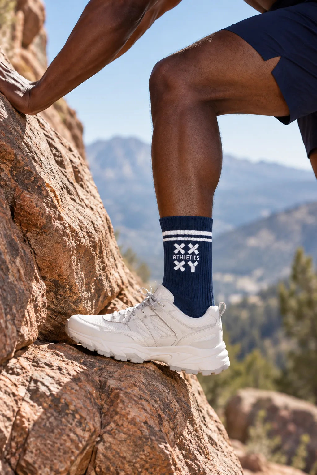 Person climbing a rock face wearing white sneakers and a navy sock with a brand logo. || navy