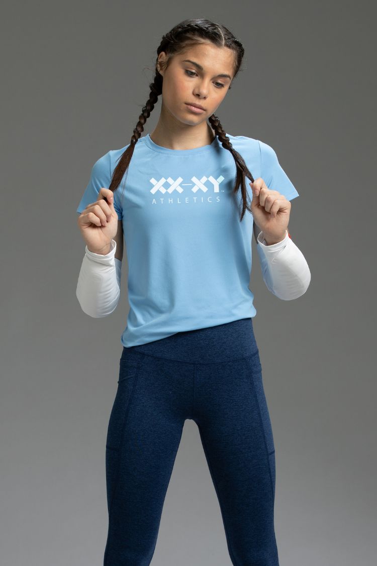Person wearing a light blue 'XX XY Athletics' t-shirt on a gray background || Light Blue