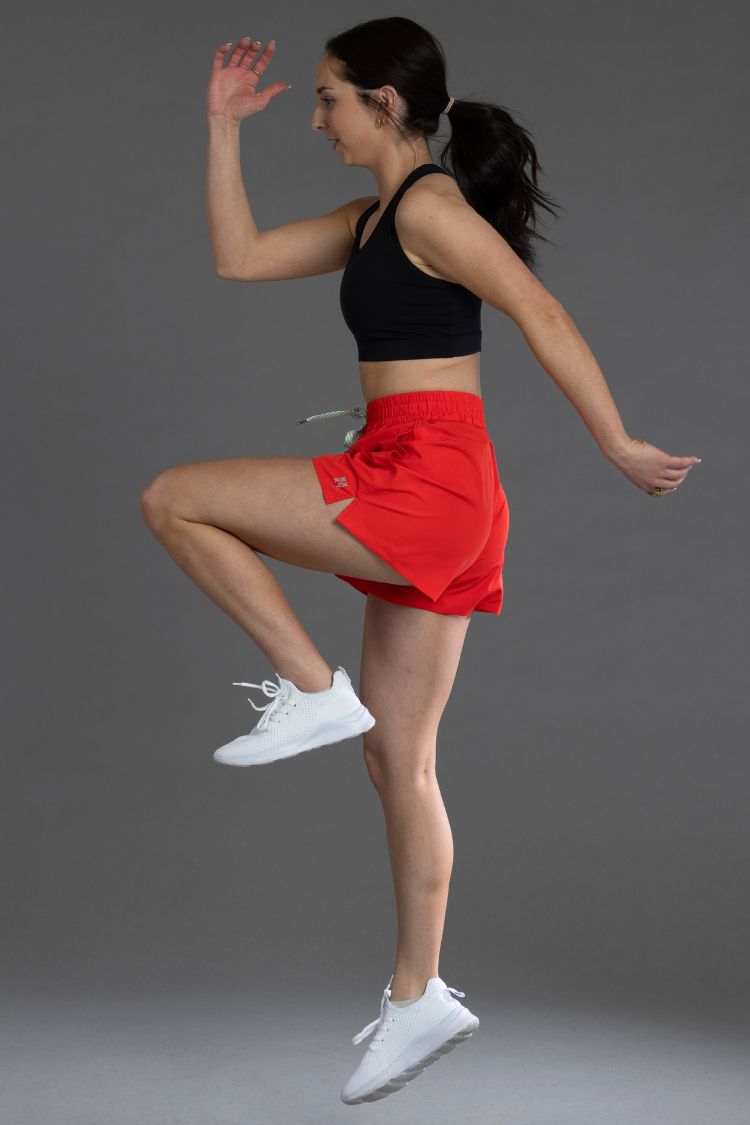 Woman in black sports bra and red shorts posing against a gray background || Red