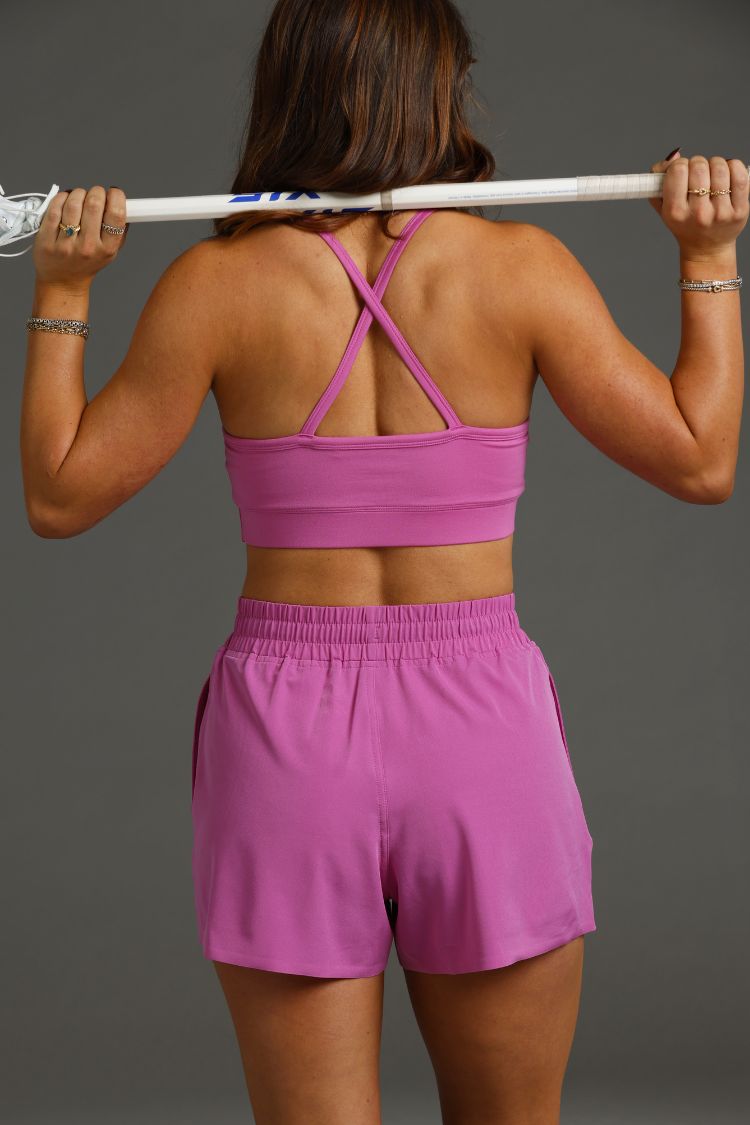 Person wearing a pink sports outfit holding a lacrosse stick || Bright Fuchsia