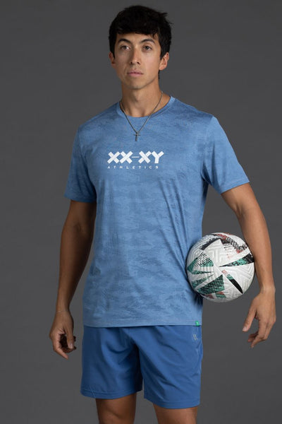 Person wearing a blue 'XX-XY Athletics' t-shirt and shorts, holding a soccer ball on a gray background || Cobalt Blue