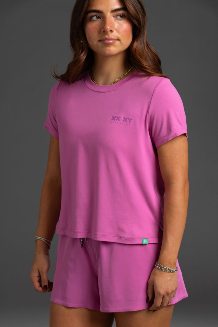 Woman wearing a pink t-shirt and shorts set with a logo on a gray background