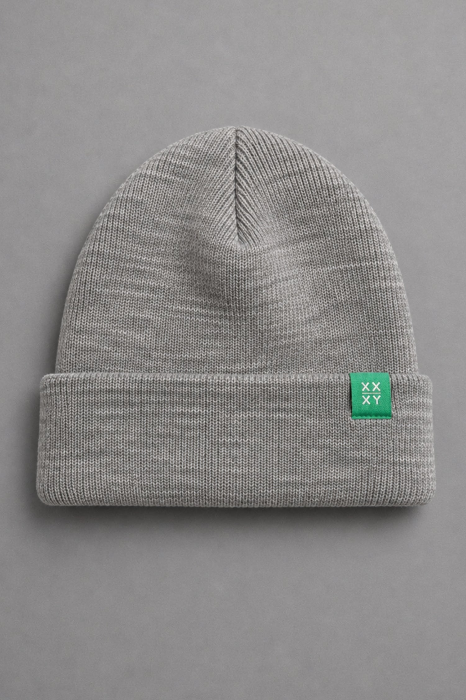 A light gray heathered knit beanie with a folded cuff, featuring a small green square patch on the side with a white logo, set against a solid gray background.