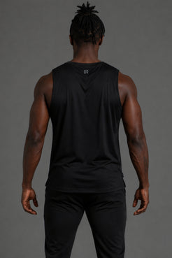 A man viewed from behind wearing a black sleeveless athletic tank top and black pants against a solid gray studio background. || Black