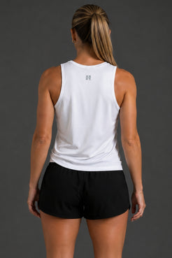 Rear view of a woman wearing a white sleeveless athletic tank top and black athletic shorts against a dark gray studio background. || White