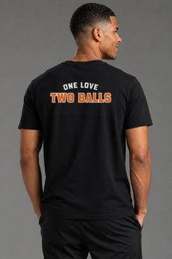 A man wearing a black t-shirt from the back, featuring the text 'ONE LOVE TWO BALLS' printed in white and orange on the back, against a solid gray studio background. || Black