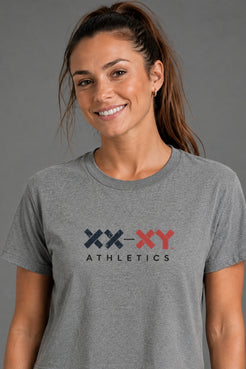 A woman modeling a heather gray cropped t-shirt with a 'XX-XY ATHLETICS' logo on the chest against a solid gray studio background. || Heather Gray
