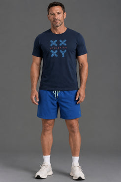 A man modeling a navy blue t-shirt with a blue graphic print and matching blue athletic shorts, standing against a solid gray studio background. || Navy Camo