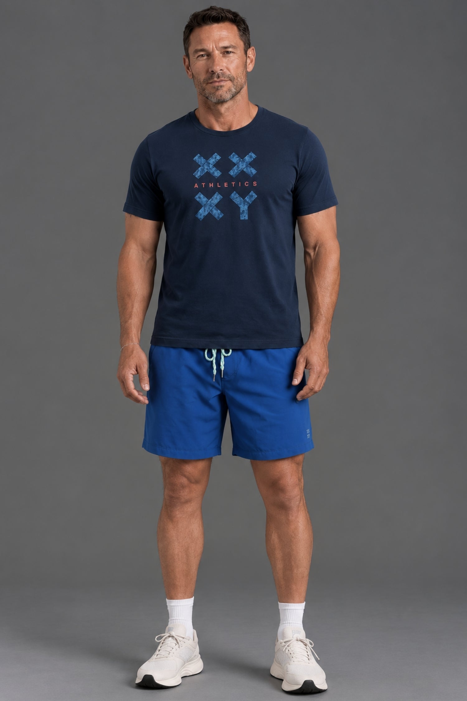 A man modeling a navy blue t-shirt with a blue graphic print and matching blue athletic shorts, standing against a solid gray studio background. || Navy Camo