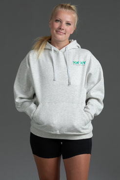 A woman modeling a light heather gray pullover hoodie with a green 'XXX YYYathletics' logo on the left chest, paired with black athletic shorts, against a solid dark gray studio background. || Light Heather Gray