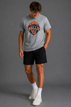 A man modeling a heather gray t-shirt with a 'Falcon Bats' graphic on the chest, paired with black athletic shorts, white socks, and white sneakers against a solid gray studio background. || Heather Gray