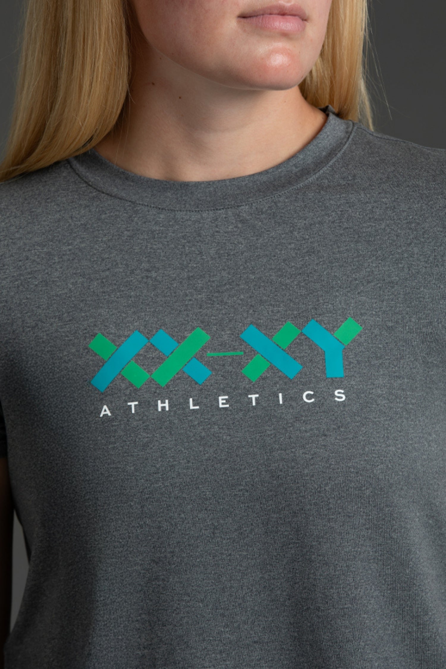 Close-up of a woman wearing a dark heather gray crewneck t-shirt with a 'XX-YYY ATHLETICS' logo printed on the chest in teal, green, and blue.