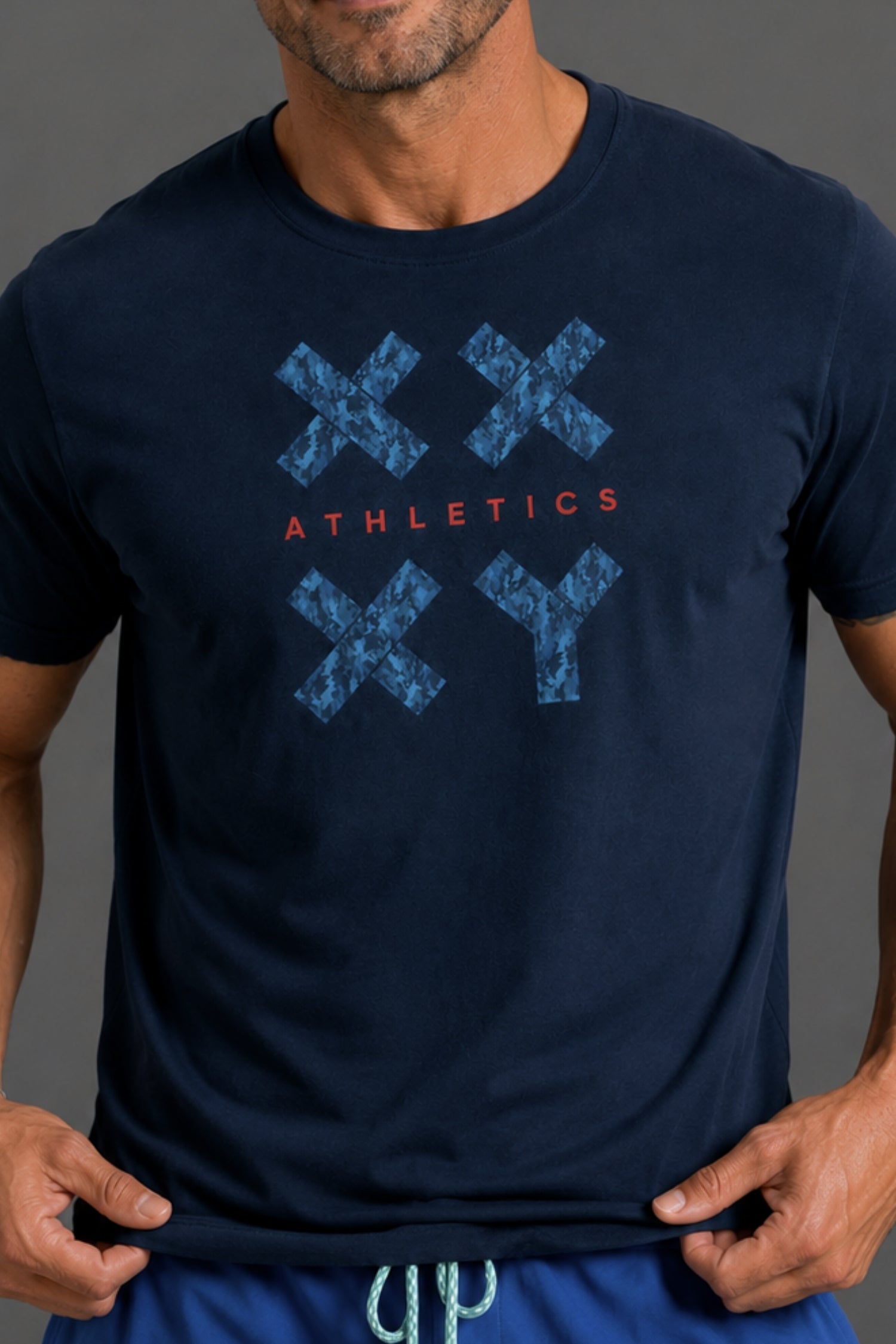A man wearing a navy blue athletic t-shirt with a blue distressed 'XXYY' graphic and the word 'ATHLETICS' in red across the chest.