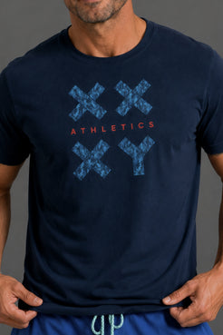 A man wearing a navy blue athletic t-shirt with a blue distressed 'XXYY' graphic and the word 'ATHLETICS' in red across the chest. || Navy Camo