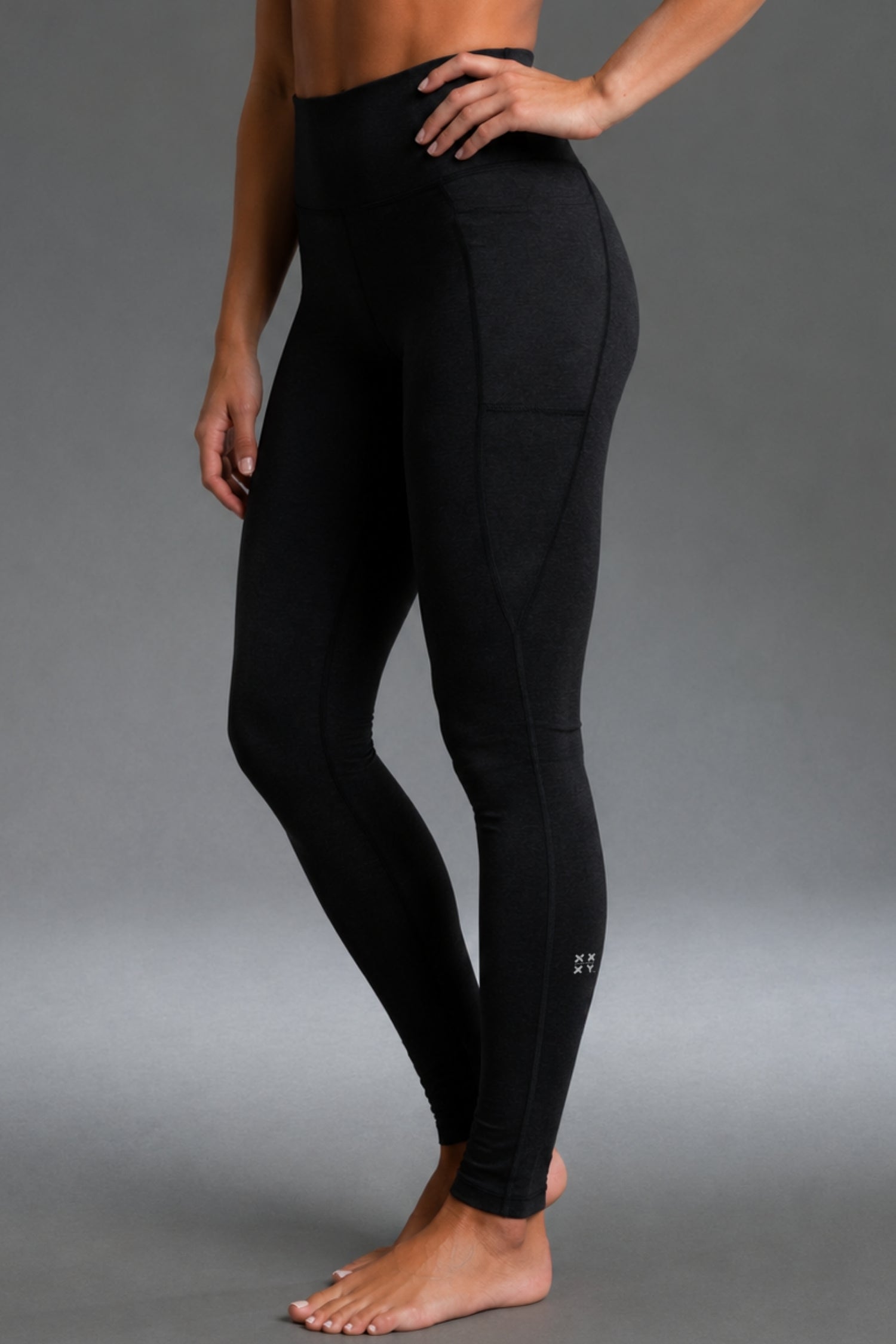 A model wearing black high-waisted athletic leggings with a side pocket, shown from the waist down against a neutral gray studio background. || Black Heather