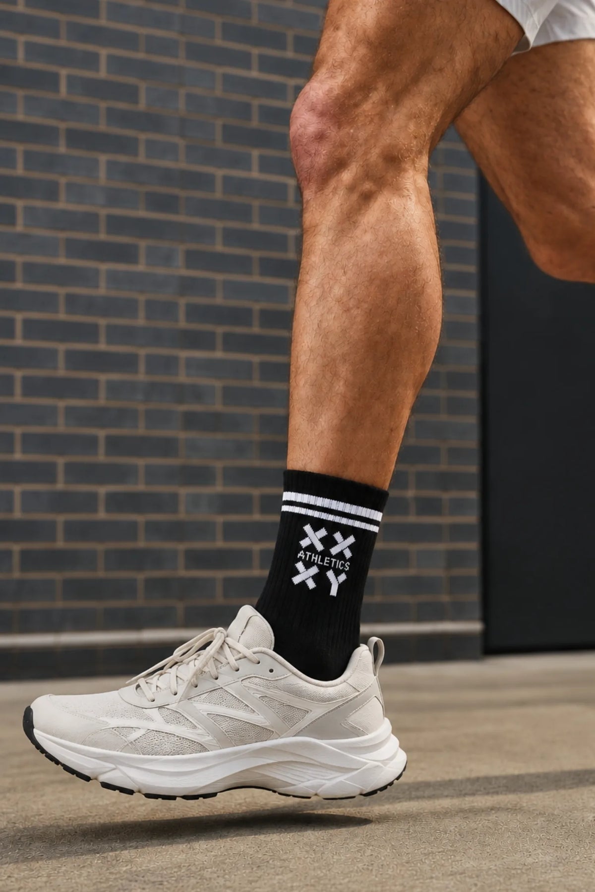 Male runner wearing black XX-XY Athletics crew socks with white stripes and neutral running shoes during an outdoor run.