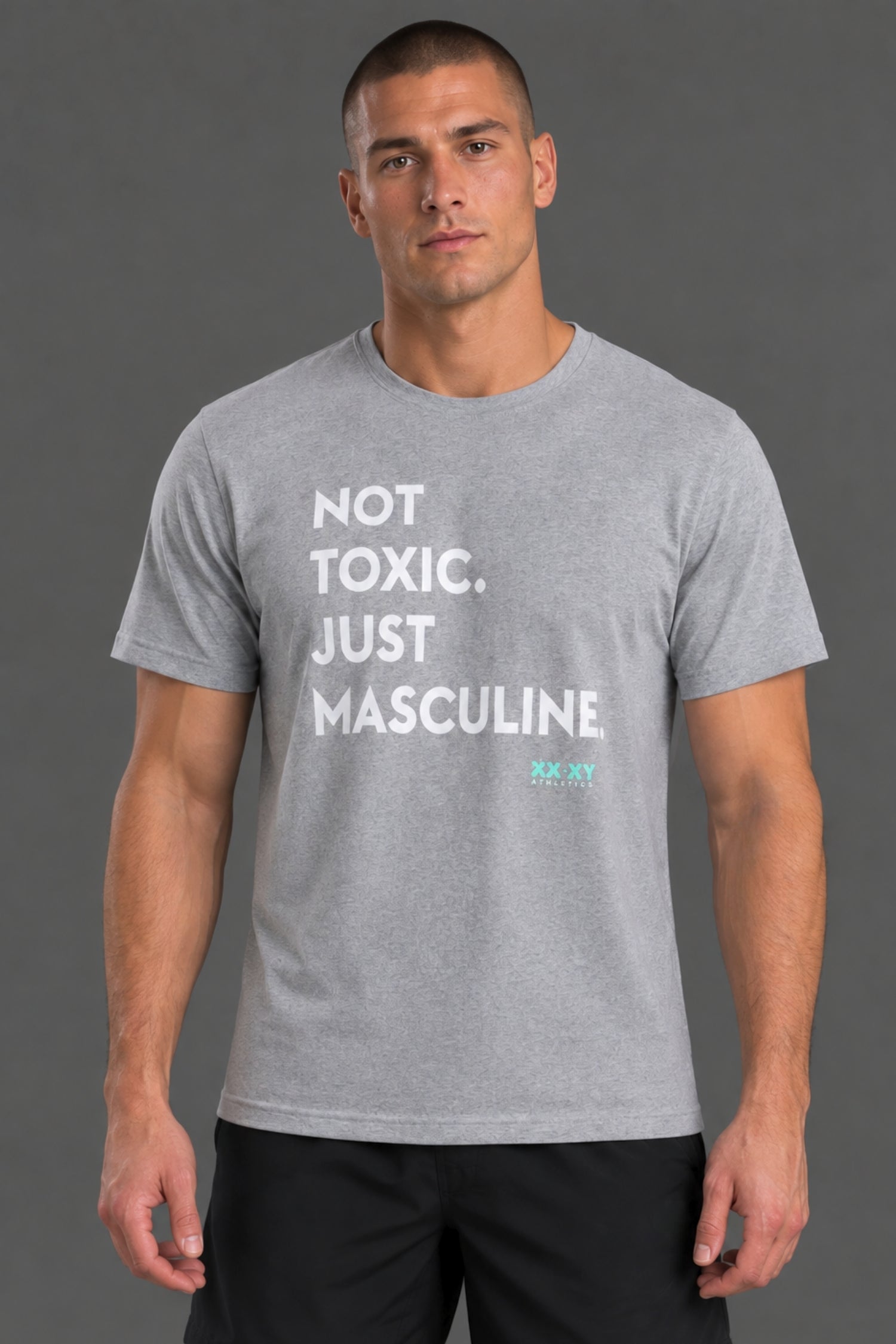 Male model wearing a gray “Not Toxic. Just Masculine.” graphic T-shirt with black shorts against a gray studio background.