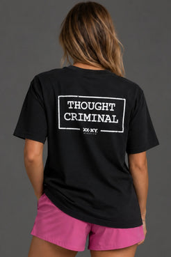 Female model wearing a boyfriend-fit black Thought Criminal graphic tee with pink athletic shorts. || Black