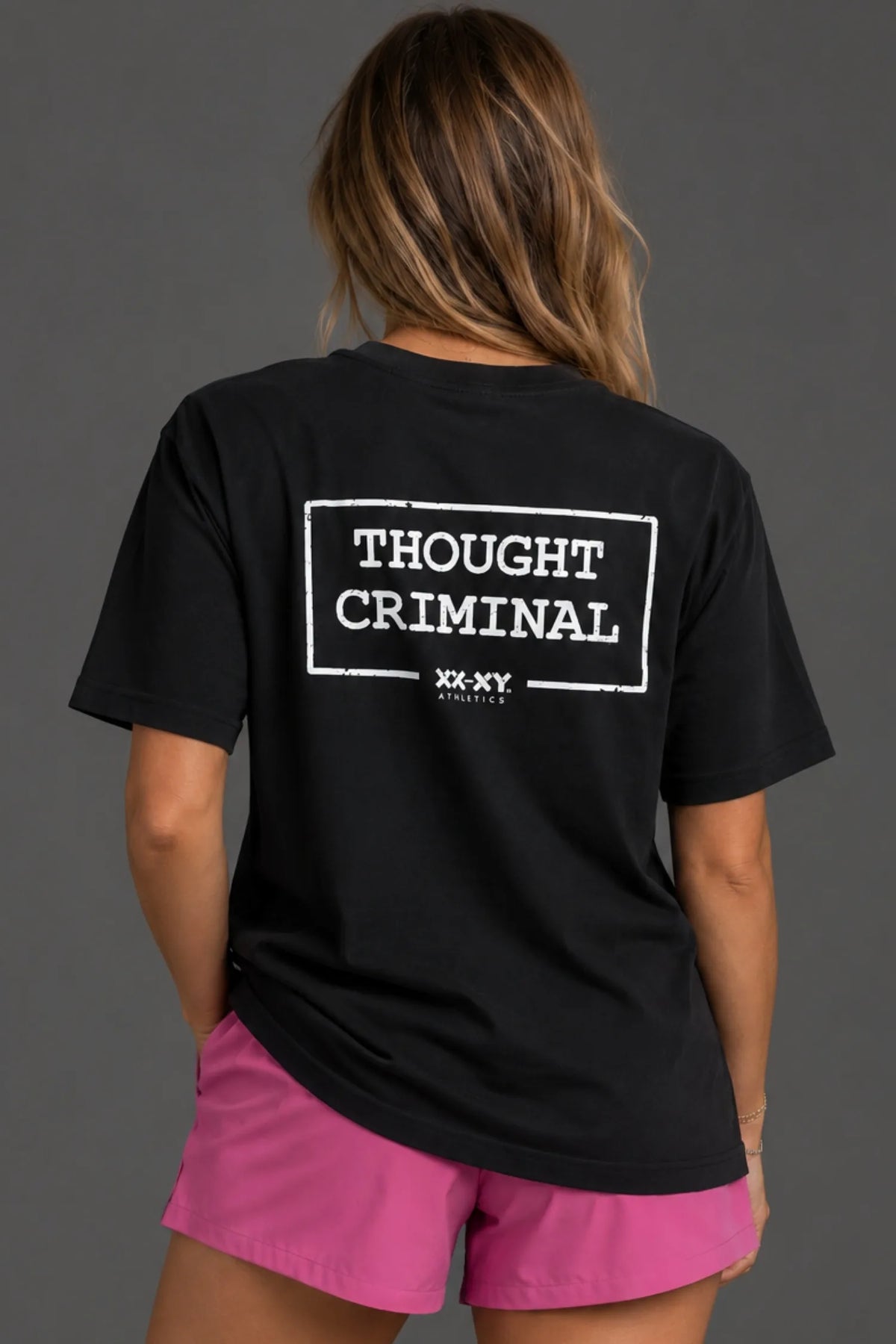 Female model wearing a boyfriend-fit black Thought Criminal graphic tee with pink athletic shorts. || Black