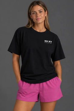 Female model wearing a boyfriend-fit black XX-XY Athletics tee with pink athletic shorts. || Black