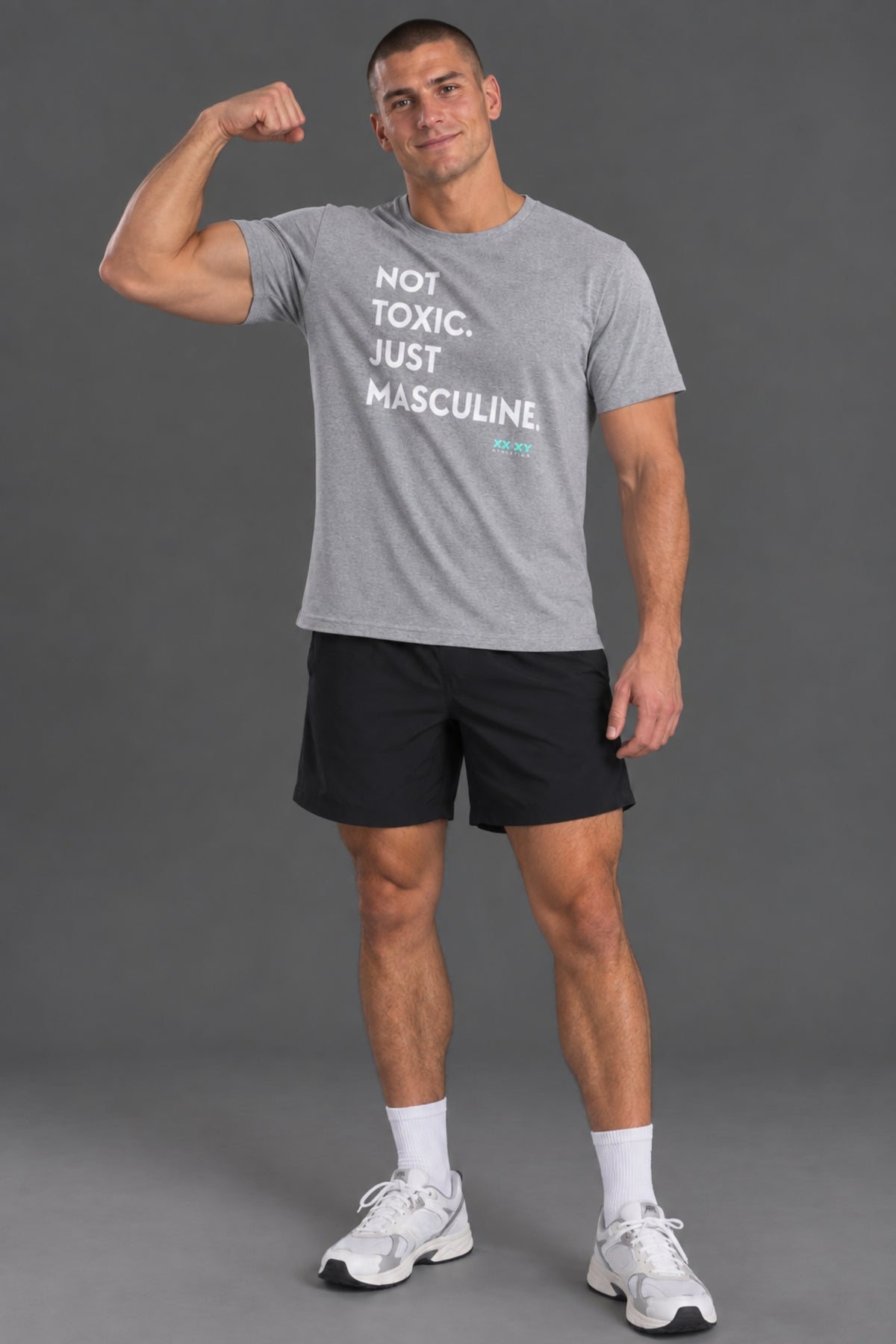 Male model wearing a gray “Not Toxic. Just Masculine.” graphic T-shirt with black shorts against a gray studio background.