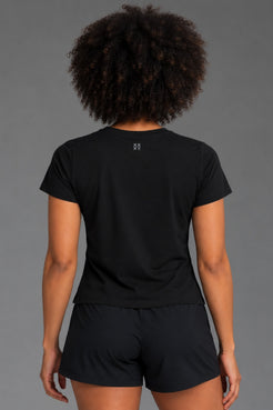 Back view of woman wearing a black XX-XY Athletics tee, showing the small gray XX-XY logo below the neckline. || Black
