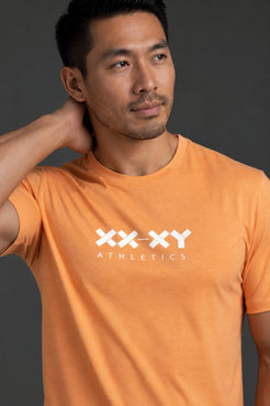 Male model wearing the XX-XY Athletics orange logo tee against a dark gray background. || Light Orange