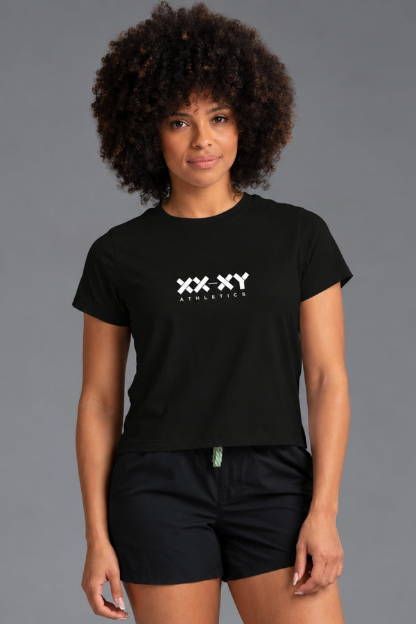 Woman wearing a black XX-XY Athletics logo tee with black athletic shorts against a gray studio background. || Black